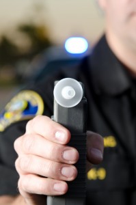 A police officer holds the breath test machine for a suspect to blow into with a police car in the background. *The police officer was blurred on purpose.